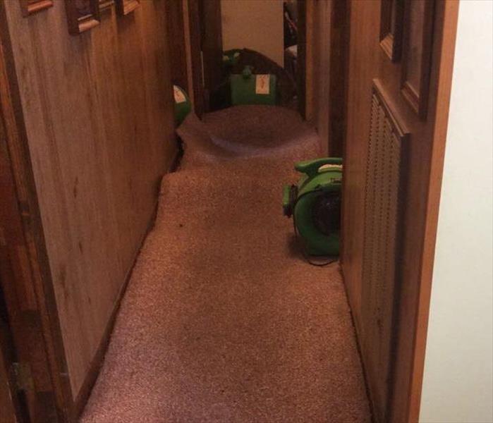 Carpet in a hallway lifted up with green drying equipment under the carpet