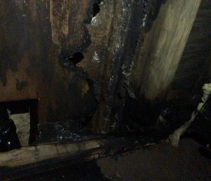 A crawlspace that has been affected by a faulty plug in the laundry room. The wood is charred and black. 