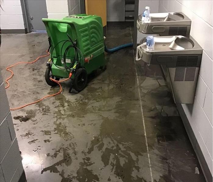 A hallway with two water fountains and a green dehumidifier with water all over the floor.