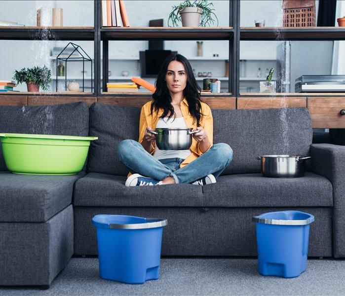 Beautiful woman with pots and buckets dealing with water damage in living room